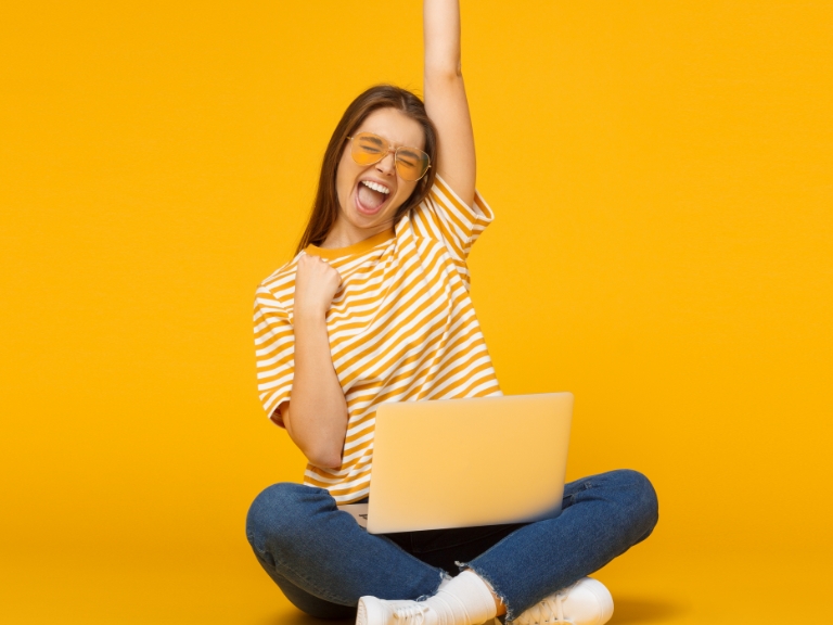 happy woman raising her arm in a cheer with a laptop on her lap