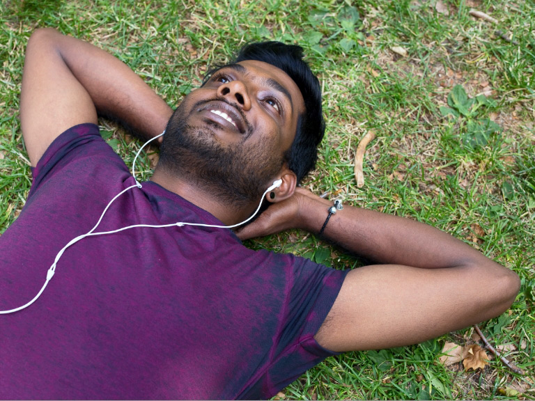 young Indian man relaxing in the park listening to music